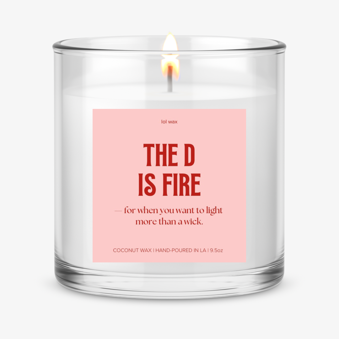 lol wax's 'The D is Fire' candle with a sassy pink label, a flame softly glowing, setting a flirty mood.