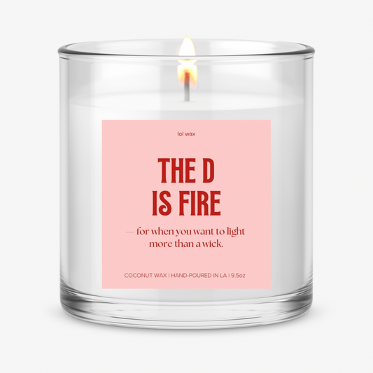 lol wax's 'The D is Fire' candle with a sassy pink label, a flame softly glowing, setting a flirty mood.