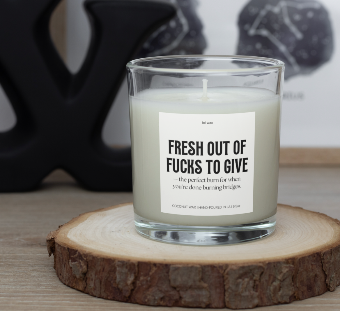 Fresh Out of Fucks to Give' candle by lol wax displayed on a wood slice, complementing a contemporary and stylish setting.