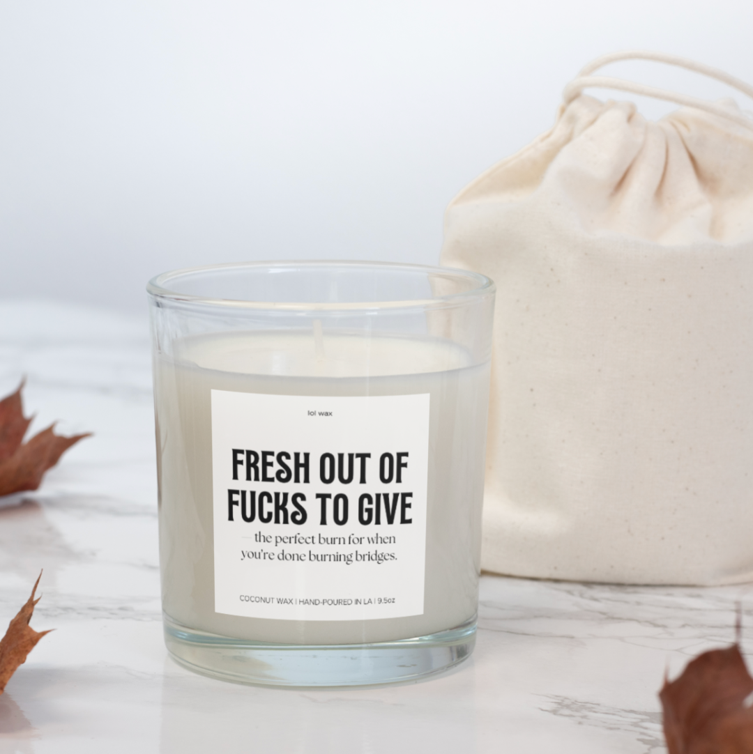 Fresh Out of Fucks to Give' candle by lol wax on a marble countertop next to a natural canvas pouch, blending modern and rustic decor.