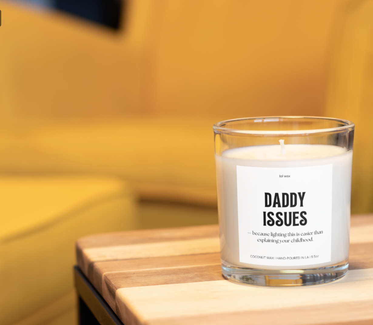 The 'Daddy Issues' candle by lol wax on a wooden surface, offering a warm, inviting ambiance with its soft glow and humorous label.