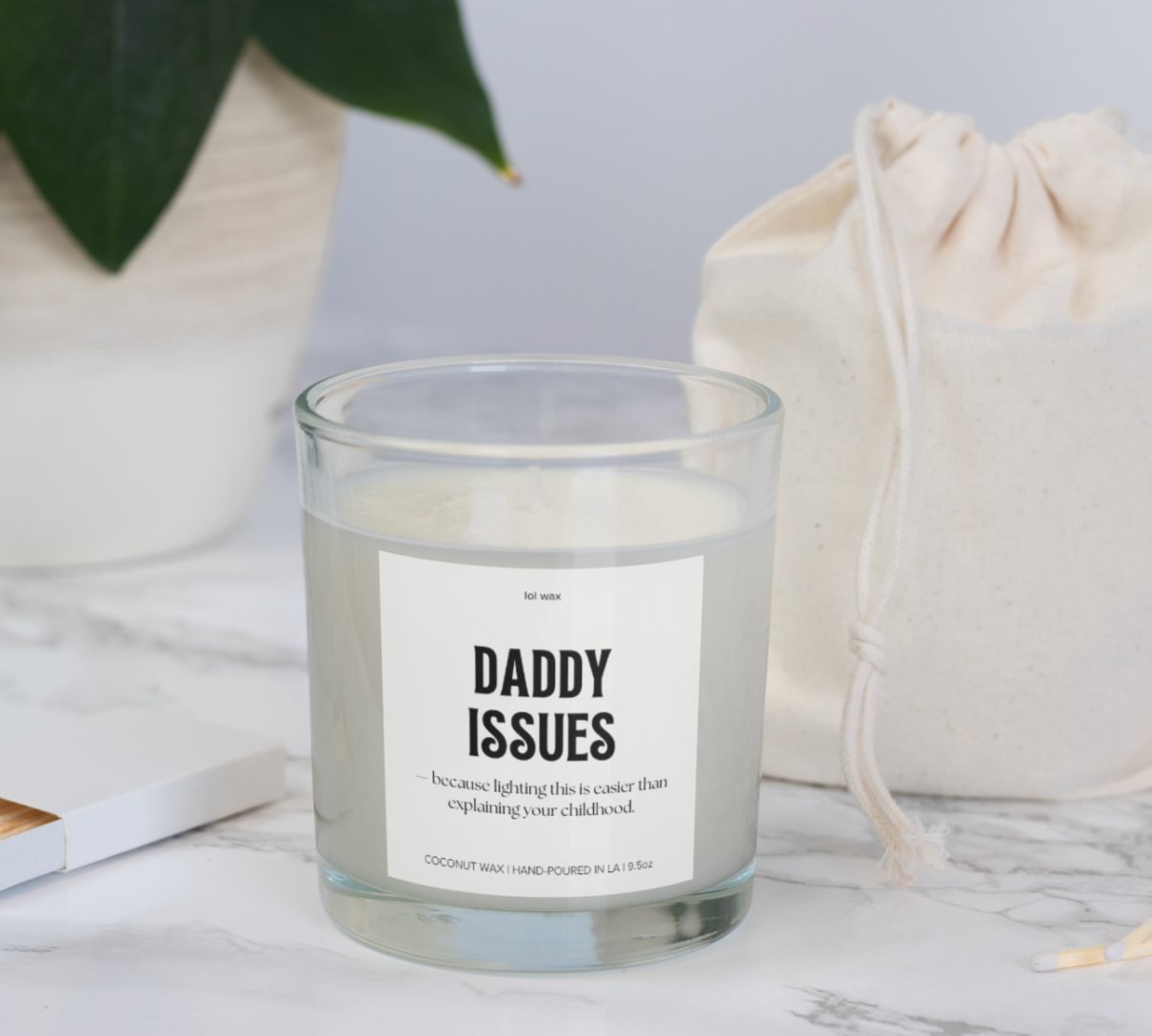 Elegant 'Daddy Issues' candle by lol wax on a marble background next to a natural fabric pouch, blending sophistication with a touch of humor.